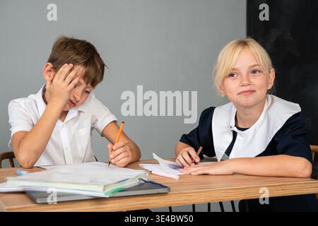 Children School Classroom Study - Boy and girl sitting at a desk in a classroom, the boy looks frustrated and the girl looks confident. Stock Photo