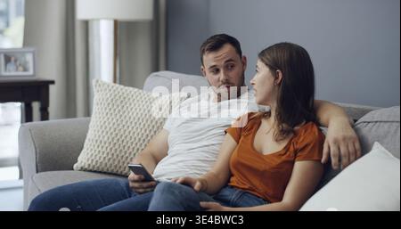 Argument, phone and couple on sofa in home with relationship problem, cheating or affair conflict. Fighting, conversation and man with woman for Stock Photo