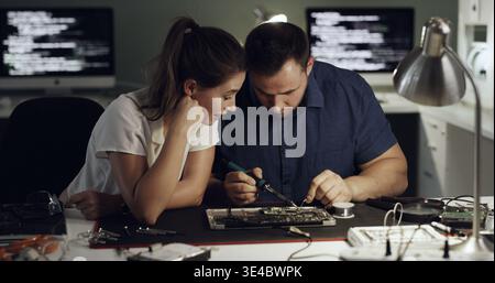 Night, motherboard and team with welding for IT maintenance, repair and diagnostics for hardware. Technology, technician and engineer people with Stock Photo