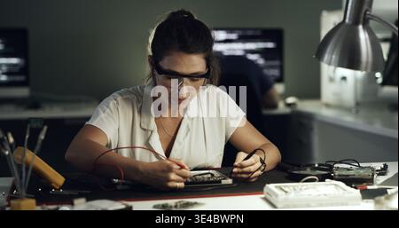 Soldering, woman or circuit repair in office for hardware diagnostics, PCB maintenance or electronics. Night, technician and multimeter probe on Stock Photo