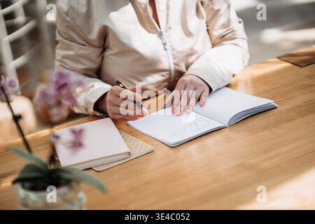 Hands Writing In Paper Notebook With Pen: Close Up Of Note Taking On Wooden Table In Natural Light. Copywriting Stock Photo