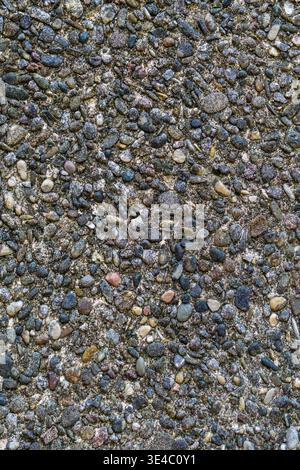 Close up of dark gravel embedded in concrete forming a dense textured surface. Stock Photo