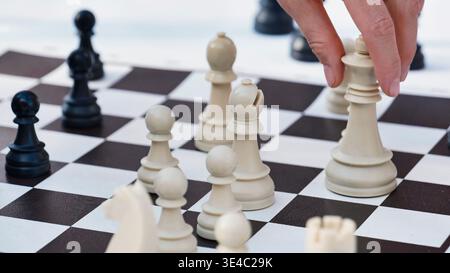 Close up of a hand making a strategic move with a white chess piece on a board. Stock Photo