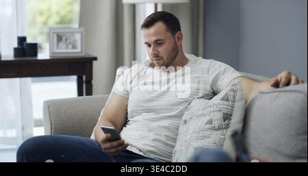 Man, relax and reading on couch with phone, text message notification and website for news on weekend. Person, chill and scroll in home with tech Stock Photo