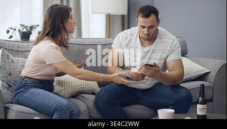 Couple, argument and cheating affair with phone on sofa for private messages or secret in home. Man, woman and spying on mobile smartphone or couch Stock Photo