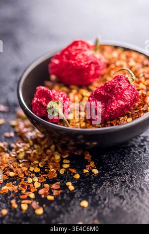 Dried red chili peppers and crushed red pepper flakes arranged in a bowl on a dark textured surface, suggesting spicy flavor, rustic cooking, bold col Stock Photo