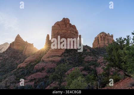 Starburst sun setting behind red rock formations Stock Photo
