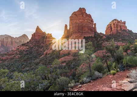 Starburst sun setting behind red rock landscape Stock Photo