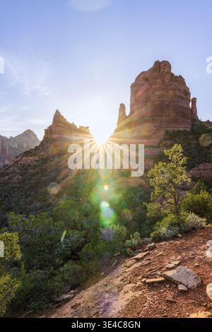 Sunburst flare sun setting behind red rock formations Stock Photo