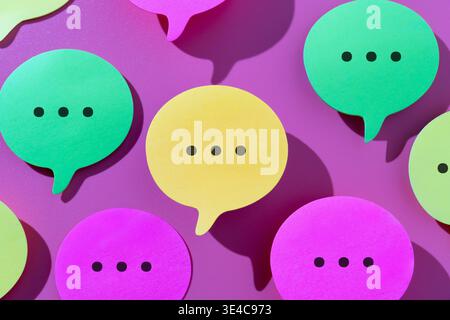 A top-down view of colorful paper speech bubbles containing ellipsis dots. Communication, social media chat, online networking, and digital messaging Stock Photo