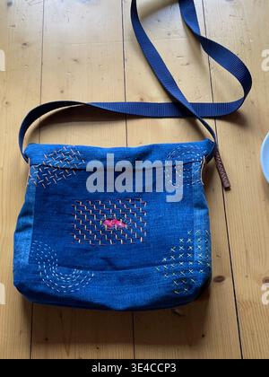 Close-up of a blue denim bag with traditional Sashiko embroidery repair, mended hole highlighted in pink thread Stock Photo