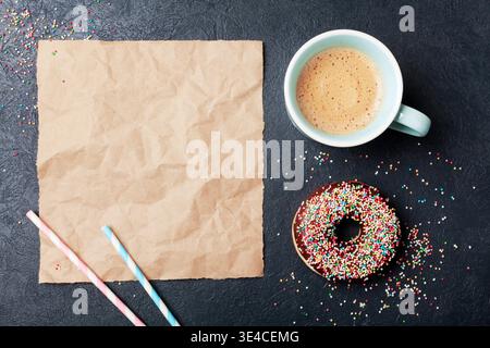 Colorful donut with cup of coffee on black table top view. Flat lay. Paper sheet for text. Stock Photo