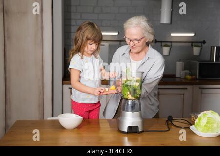 Healthy nutrition in the family, vegetarianism. Senior lifestyle. grandmother and granddaughter drink smoothie from greenery and superfoods in the kitchen at home || Model released Stock Photo