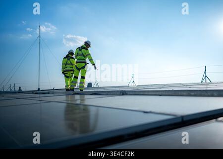 Male and female engineers inspecting rooftop solar panels on a modern building, representing solar energy, clean power, and sustainable urban development || Model released Stock Photo
