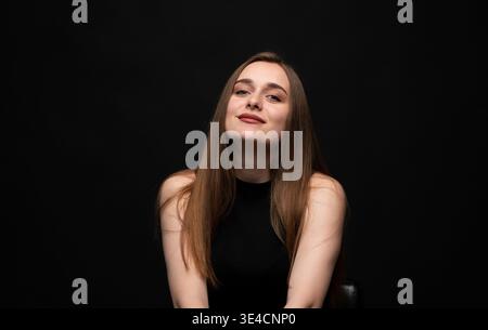 Young woman with long brown hair smiling on black background, presenting beauty, confidence, and lifestyle Stock Photo