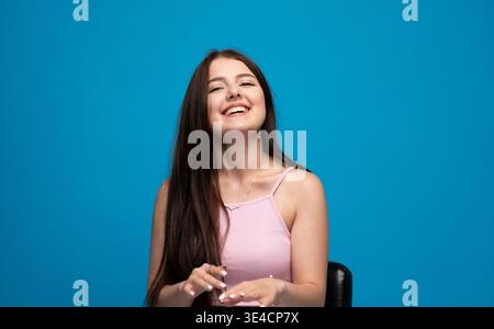 Smiling young woman posing with happy expression on blue background, enjoying her free time and a positive mood Stock Photo