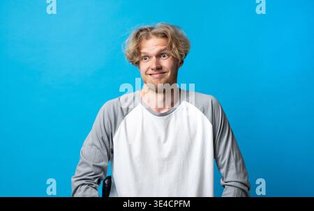 Confused young man feeling uncertain and doubtful, having a skeptical and wary facial expression showing awkwardness and thinking on a blue background Stock Photo