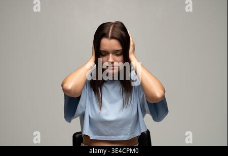 Young woman feeling overwhelming noise and pain, eyes closed, covering ears to block out sound and minimize distraction Stock Photo