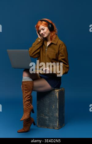 A red haired woman in spring fashion sits against a blue background. Stock Photo