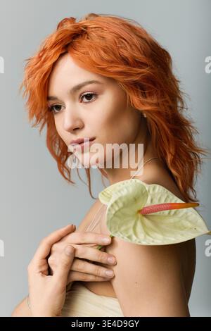 A young woman with red hair embodies spring in a strapless dress against a grey background. Stock Photo