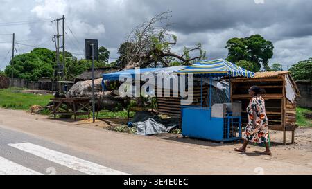 A woman walking in the foreground with traditional African villages in the background, captured candidly from a moving vehicle. Stock Photo