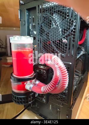 Custom PC liquid cooling system featuring red coolant, flexible transparent tubing, and an external D5 pump with reservoir mounted on a black gaming c Stock Photo