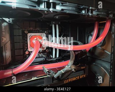 Interior view of a high-performance gaming PC featuring a custom liquid cooling loop with red fluid, CPU water block, RGB lighting, and an NVIDIA GeFo Stock Photo
