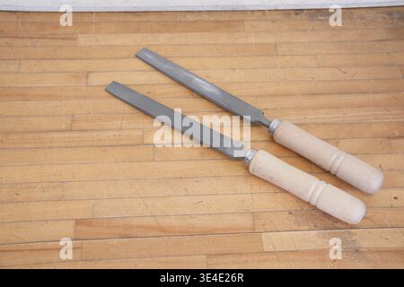 Two hand files rest on a warm wooden floor. Handles are light-colored, smooth, and gently curved. Metal surfaces show fine, textured grooves for preci Stock Photo