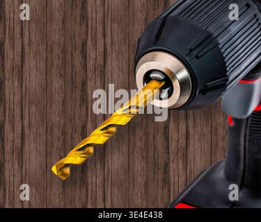 Close up of a golden colored drill bit in a cordless drill. Wood panel background. Stock Photo