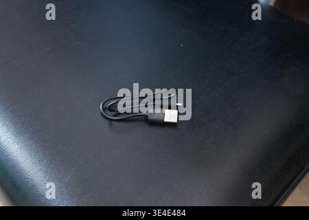 Coiled USB cable rests on black textured surface. Minimalist design shows tech simplicity and utility. Ideal for digital or gadget-themed content. Cab Stock Photo
