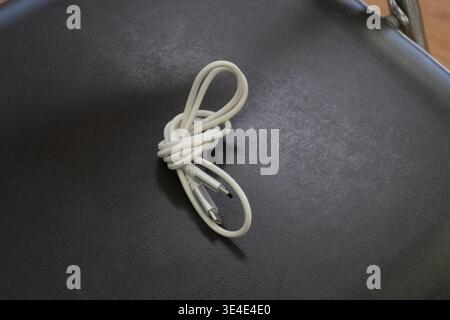 Coiled white cable rests on dark textured surface. Simple, clean composition draws attention to cable's form. Minimalist style suits tech, design, or Stock Photo