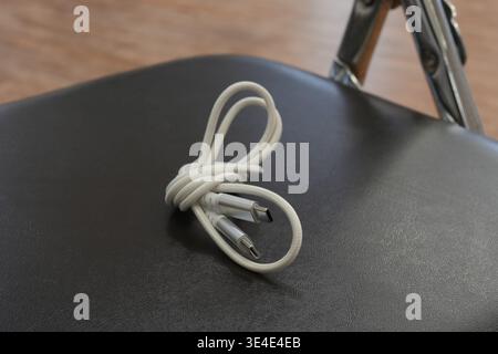Coiled cable rests neatly on dark surface. Soft lighting highlights cable's texture and shape. Background shows minimalistic setup with tripod leg. Ca Stock Photo