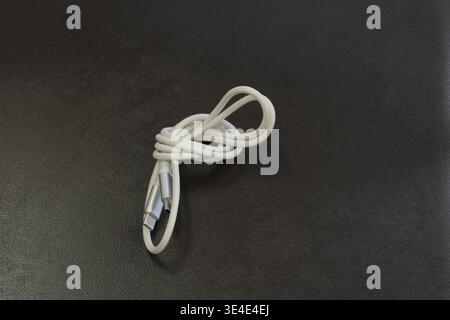 Coiled white cable rests on dark surface. Simple, clean setup draws attention to cable's form. Smooth texture contrasts with matte background. Ideal f Stock Photo