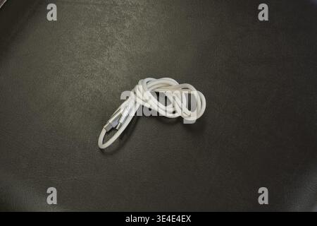 Coiled white cable rests on dark textured surface. Simple, clean composition draws focus to cable. Ideal for tech, repair, or minimalist design projec Stock Photo