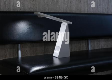 Minimalist lamp rests on sleek black bench. Modern design emits soft, focused light. Clean lines suggest contemporary style. Ideal for study, work, or Stock Photo