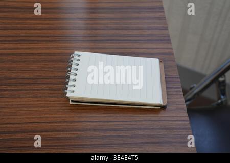 Small notebook rests on warm wooden table. Metal spiral binding holds neat lined pages. Soft light highlights texture of cover and grain. Minimalist s Stock Photo