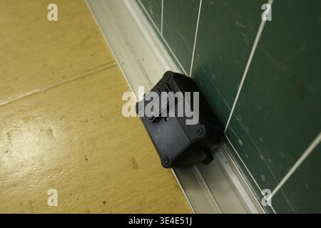 Black box rests against green tiled wall. Yellow floor meets white baseboard. Simple, clean, industrial design. Utility or tech equipment shown. Great Stock Photo