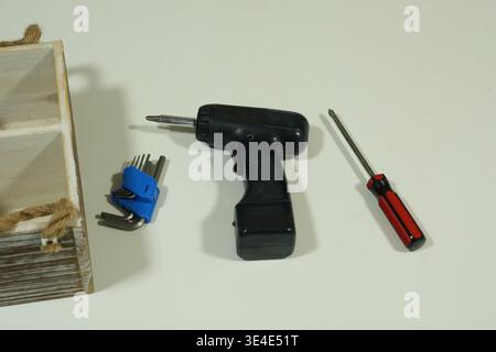 Wooden box holds tools neatly arranged. Black drill and red screwdriver lie side by side. Blue socket wrench set adds practical detail. Bright surface Stock Photo