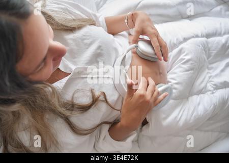 Pregnant woman placing headphones on her belly, sharing music with her unborn child Stock Photo