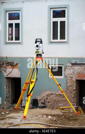Geodetic surveying instrument on tripod at construction site, used for measurement and planning during building renovation and engineering work. Stock Photo