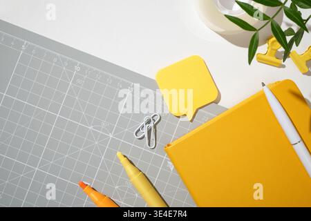 Yellow notebook, pen, highlighters, and a speech-bubble sticky note on grey cutting mat. Copyspace Stock Photo