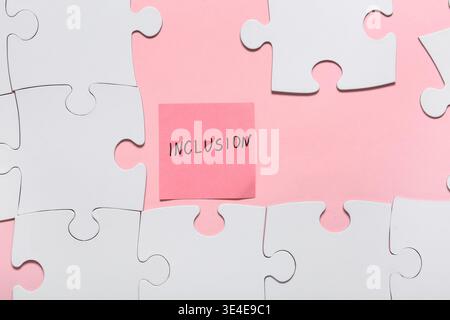 Paper with word INCLUSION and puzzle pieces on pink background Stock Photo