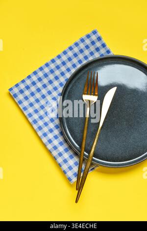 Empty plate with cutlery and blue checkered napkin on yellow background Stock Photo