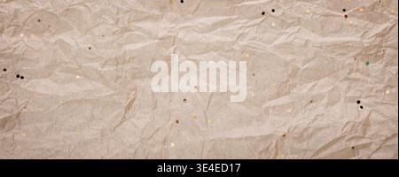 Crumpled kraft paper scattered with colorful tiny glitter particles, banner format Stock Photo