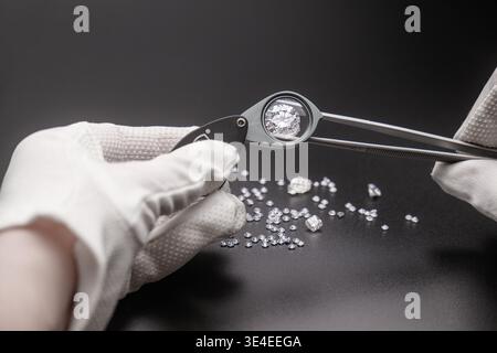 Hand holds magnifying glass over diamond. Other diamonds scattered nearby Stock Photo