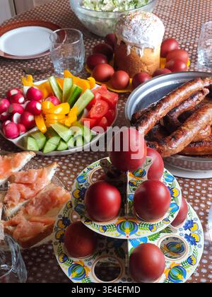 Easter lunch with dyed red eggs, sausages, cucumbers, tomatoes, radishes, sandwich on plates on a stand Stock Photo