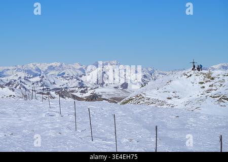 Three hikers reaching snowy mountain peak Schießeck summit cross, Lachtal ski resort, Austria. Stock Photo