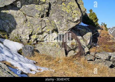 Coiled rusty barbed wire in a rugged mountain landscape. Stock Photo