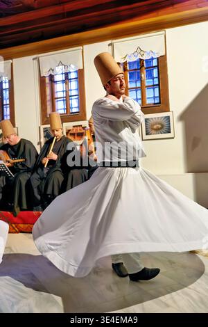 Dancers in white robes spin in a ceremony in Istanbul. Musicians play traditional instruments in the background. Stock Photo