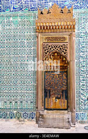 Visitors notice a historical water fountain inside Topkapi Palace in Istanbul. The fountain features intricate designs and colorful tiles. Stock Photo